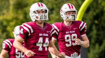 Image shows two football players in uniform running onto the field for a game. 
