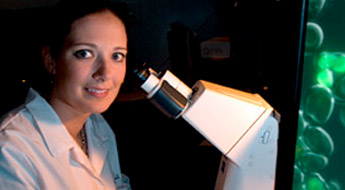 Image shows student smiling as she prepares to use a high-powered microscope. 