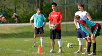 Image shows four male soccer players standing on the intramural fields with the Heritage Trail bike trail in the background. Two bike riders are passing by on the trail.