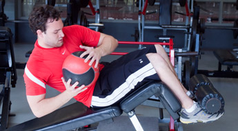Image shows male student exercising with a medicine ball while doing sit ups in the lifting room.