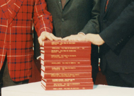 Three members of the committee with their hands on a large stack of the report