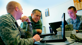 Three male ROTC students smiling and working on laptop computers.