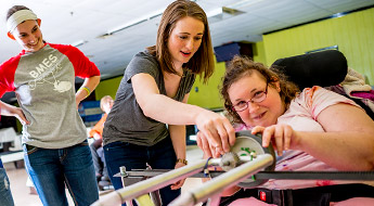 Students work with a woman using a specially designed device to enable disabled individuals to bowl.