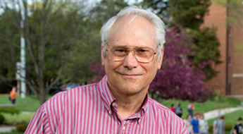 A smiling Dr. Elton Graves standing outdoors on the Rose-Hulman campus with students walking in the background