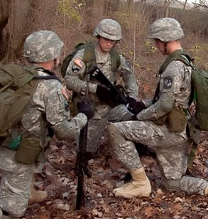 Group of three men in uniform huddle outside with their weapons.