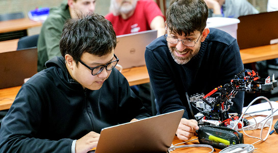 Computer Science faculty and male students working in a computer class.