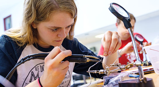 Female student uses electronic equipment to assemble a student project.