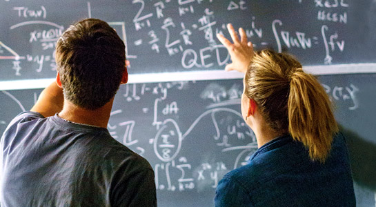 Male and female students working a math problem on a chalkboard.