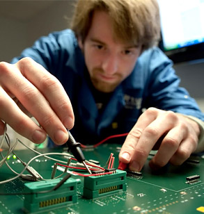 Male student uses a small screwdriver to assemble elements of a circuit board.