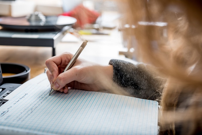 Student's hand holding a pen writing in a notebook.