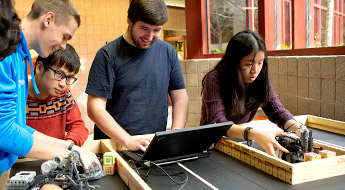 Male and female students use a laptop to set up robots on a table.