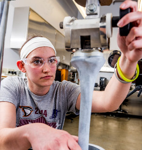 Female student wearing goggles works with apparatus