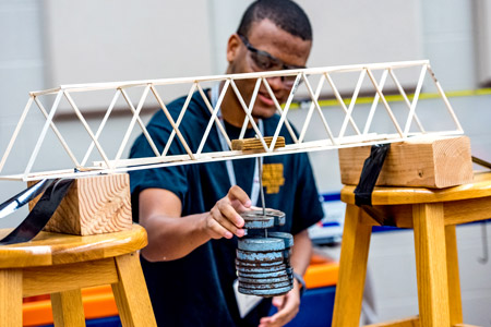 A male Catapult student working on a project involving a wooden model of a bridge