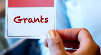 Image shows a female student’s hand as it holds a small red and white card reading ' Grants.'