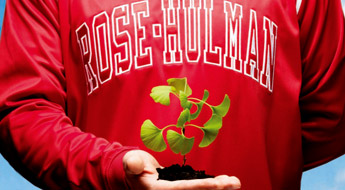  Image shows a student wearing a red Rose-Hulman sweatshirt and holding a small green plant with its roots in rich black soil.