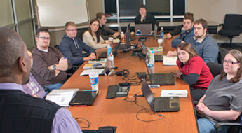large group of students sit around table with their laptops