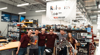 Several members of the Robotics Team posing together with a robot. 