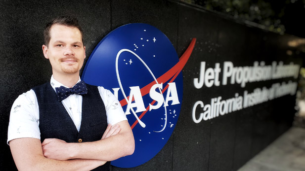 Sam Howell in a bowtie standing beside NASA Jet Propulsion Lab sign.