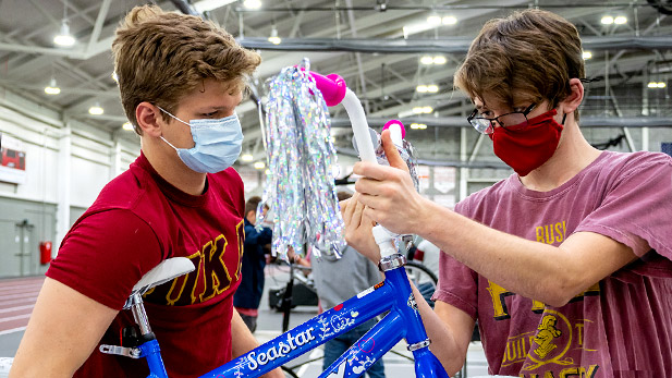 Two students wearing masks assembling a bicycle.