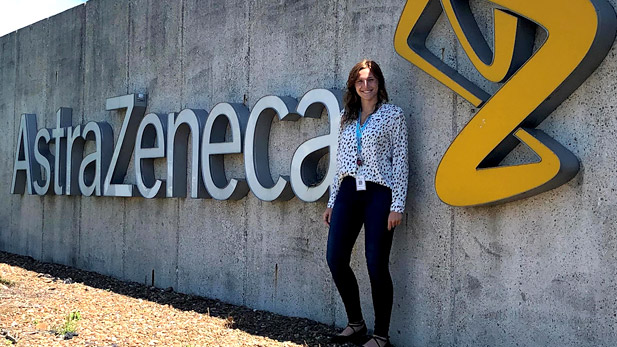 A smiling Madison Wendelin standing outside next to a sign reading AstraZeneca.