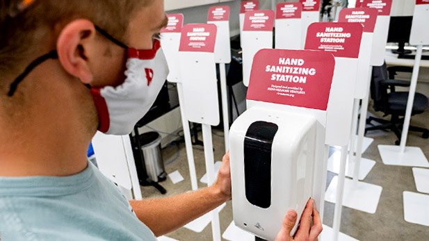 Student working on hand sanitizer station in Rose-Hulman Ventures with completed stations lined up nearby.
