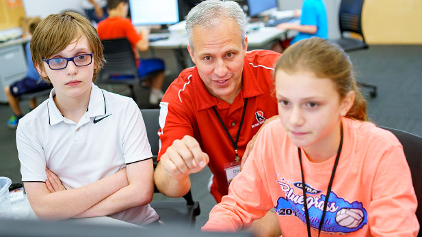 Two young students smiling and working at a computer with Dr. David Fisher.