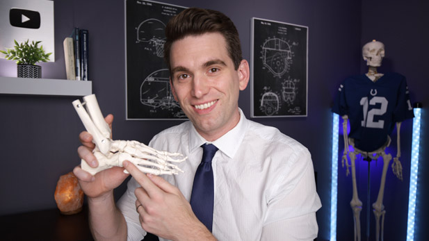 Brian Sutterer smiling and holding a human foot skeleton and pointing to the bones.
