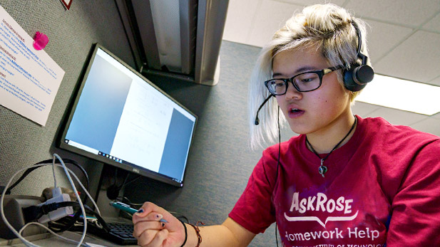 Student employee of AskRose talking on the phone while consulting a textbook to help a student caller.