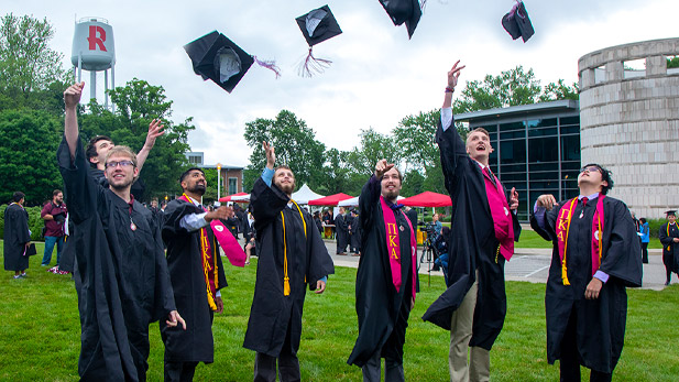 Six Rose-Hulman graduates toss their caps outside Hatfield Hall.
