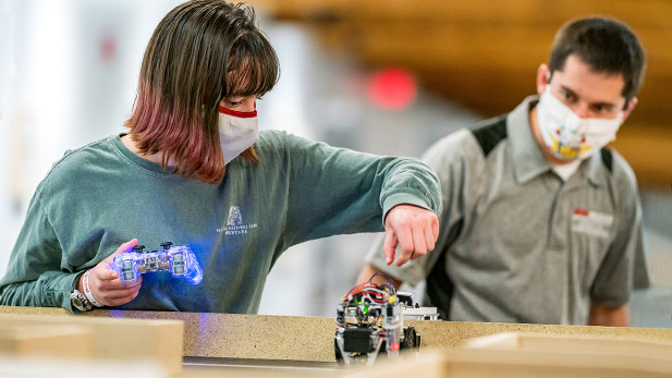Students working with a small robot as it delivers pizza. 