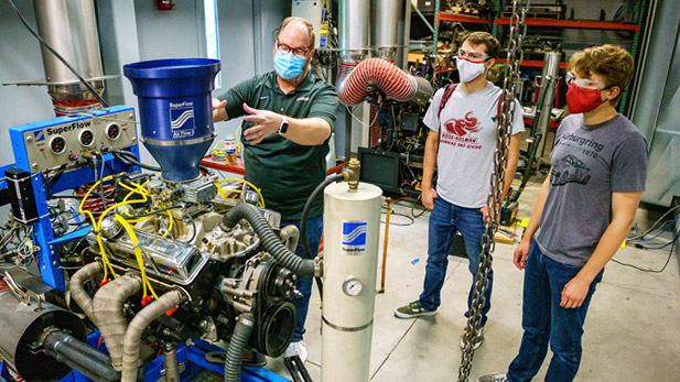 Students working in a lab with a professor giving them instructions near a piece of equipment.
