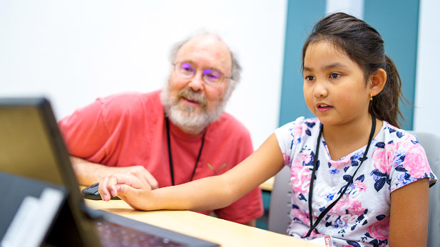 A professor works with a young girl on a computer.