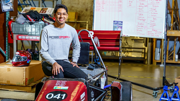 Nachi Hosahatti, wearing a Grand Prix Engineering shirt, sits on the Grand Prix Engineering car in the Branam Innovation Center.