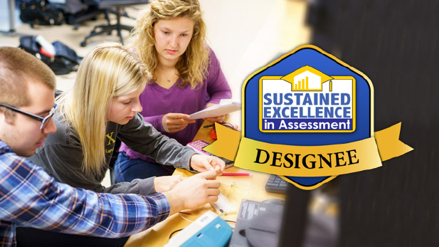 Sustained Excellence in Assessment Designee logo overlayed across an image of three students working on a project.