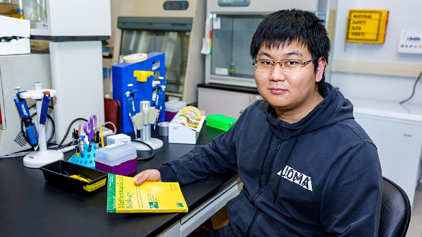 Ferguson Zhang sitting at a desk with books in a lab.