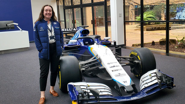 Gabbie Gilbertson stands smiling next to a race car.