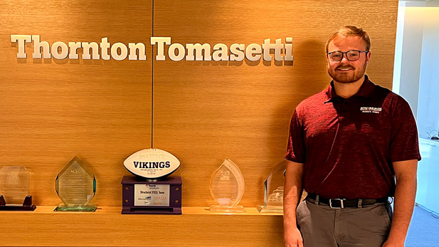Hunter Crumley standing in front of a trophy case and Thornton Tomasetti sign.