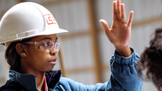 A student wearing a hard hat raises a hand.