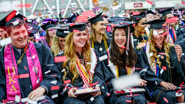 Graduates laugh and celebrate as red and white confetti falls.