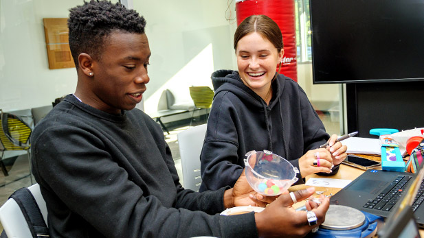 Two smiling students work on an engineering design project.