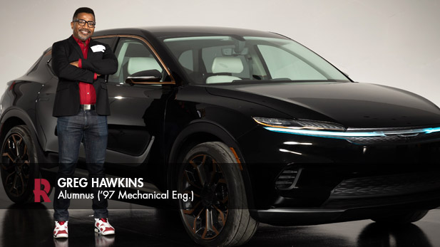 Greg Hawkins crosses his arms confidently beside a sleek black vehicle.