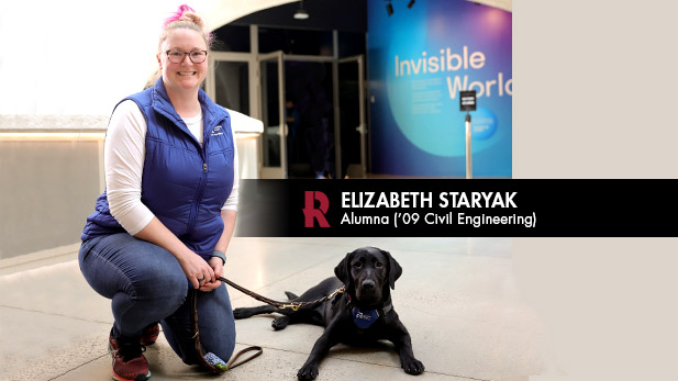 Elizabeth Staryak kneels by a black dog on a leash.