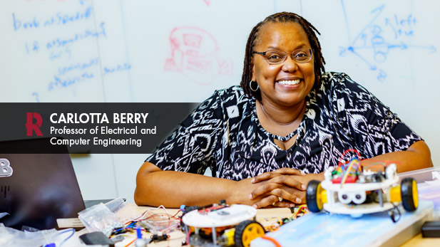 Carlotta Berry smiles behind a table covered with robots and wires.