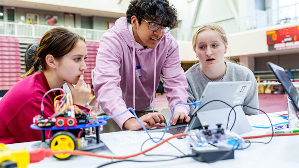 Three high school students practice problem solving with a computer and a robot.