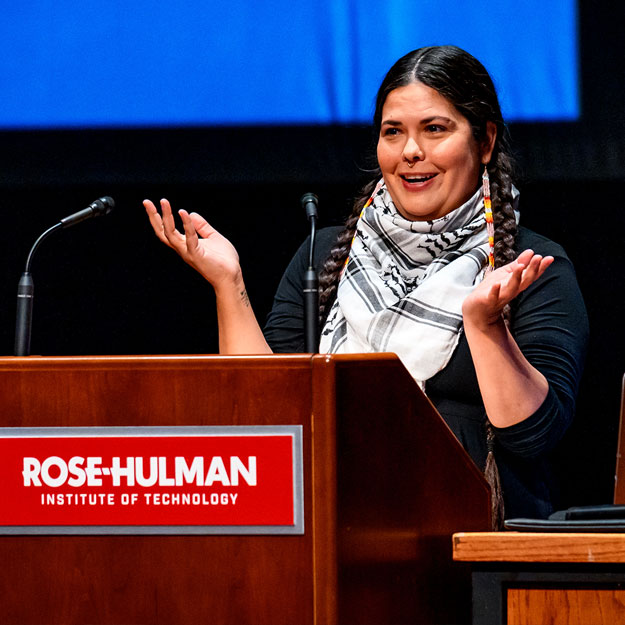 Tara Houska waves from behind a podium with a Rose-Hulman logo.
