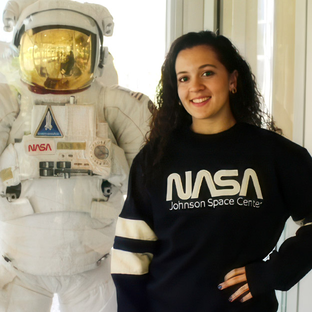 Aubrey Smith, a sophomore majoring in Mechanical Engineering, poses next to a NASA spacesuit display during her visit to the Johnson Space Center, where she is gaining hands-on experience through an internship.