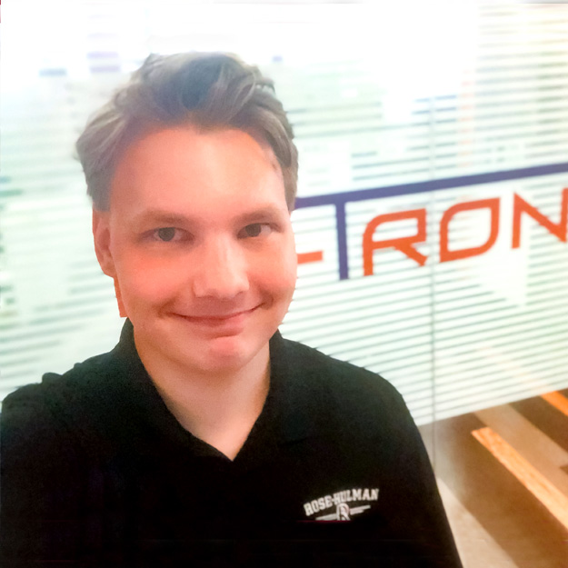 Alex Anisimov, wearing a Rose-Hulman polo, takes a selfie by a wall with the Wi-Tronix logo.