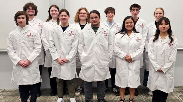 Eleven chemistry and biochemistry students proudly wear their new white lab coats, embroidered in red  on the left chest with the Rose-Hulman logo and the student's name.