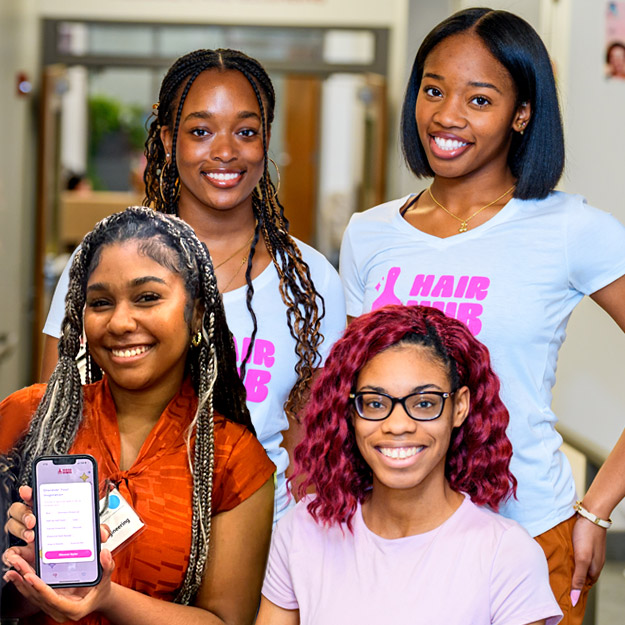 Left: Nola Wilson holds up her phone with the Hair Hub app open. Right: The three students smile, wearing pink or Hair Hub shirts with a pink logo.