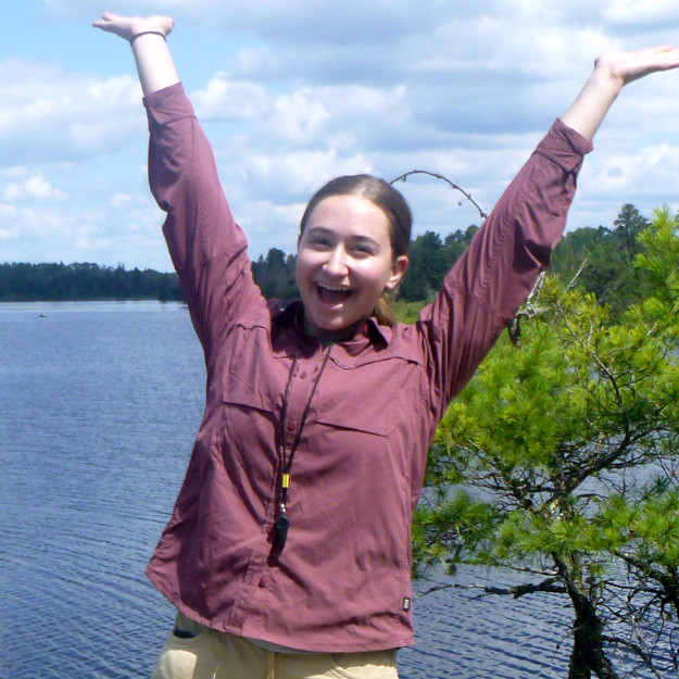 Mary Claire Obluda laughs as she clutches a fish in her gloved hands, with a body of water stretching behind her.